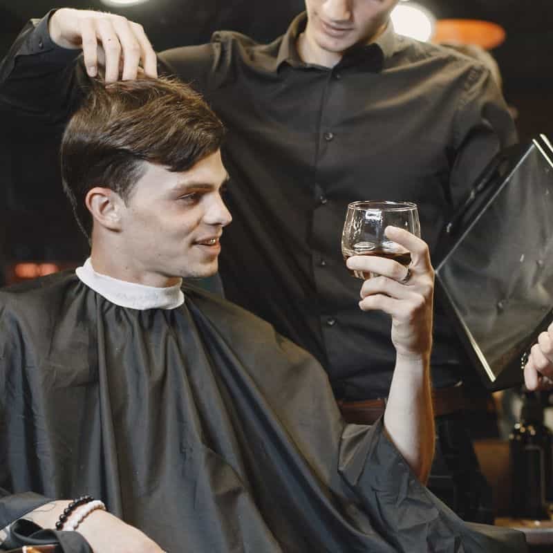 Cliente masculino relajándose en silla de barbero usando su teléfono.